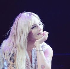 a woman with long blonde hair and tattoos on her arm sitting in front of a microphone