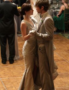 two people dressed in formal wear dancing on a dance floor with other people standing around