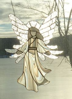 a stained glass angel ornament hanging from a chain in front of a tree