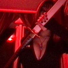 a woman holding a guitar in her right hand and singing into a microphone with red lights behind her