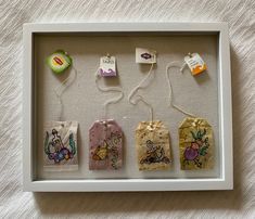 a white shadow box with four small bags and tags attached to the sides, all in different designs