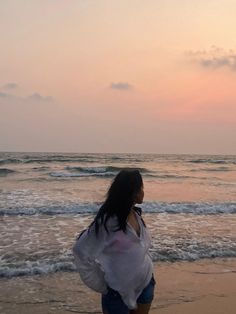 a woman standing on top of a sandy beach next to the ocean at sunset or dawn