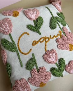 a white pillow with pink flowers and the word cappu written in cursive writing