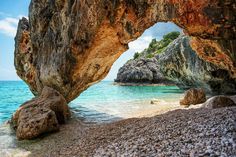 an arch in the rocks on a beach with blue water and clear sky behind it