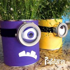 two tin cans with fake plants in them and eyes painted on the side, sitting on a counter top