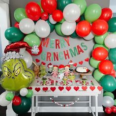 a table topped with lots of balloons next to a christmas themed sign and desserts