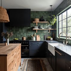 a kitchen with black cabinets and green tile backsplash, wood countertops, and open shelving