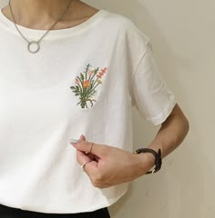 a woman wearing a white t - shirt with flowers on the pocket and a necklace around her neck