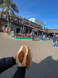 a person is holding two donuts in their hand on the street with people walking around