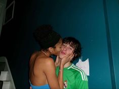 two young women kissing each other in front of a blue wall