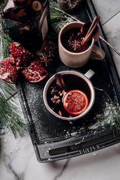 two mugs of hot chocolate with cinnamon and pomegranate on a tray