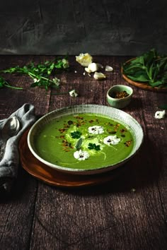 a bowl filled with green soup on top of a wooden table next to other vegetables