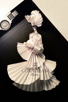 a woman in a dress made out of folded paper on top of a black table