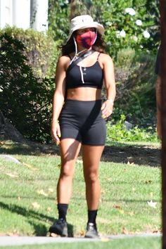 a woman in black shorts and a hat standing on the grass with her face painted red