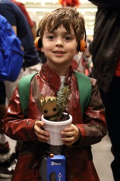 a young boy wearing headphones and holding a cup with a small plant in it