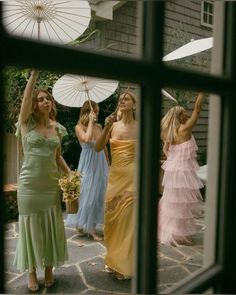 four women in dresses are holding umbrellas and looking out the window at something outside