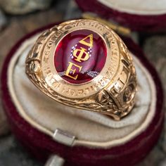 This 1941 class ring from George Washington University features an oval bufftop lab created ruby with the Delta Phi Epsilon Greek letter gold inlays and detailed gold work on the shoulders. The ring is crafted in 10k yellow gold with a light patina and is currently a size 8.75. The initials JJD are hand engraved inside the shank. Classic Ruby Ring With Polished Finish For Collectors, Ceremonial Heirloom Oval Ruby Ring, Red Oval Engraved Ring With Polished Finish, Luxury Engraved Oval Ruby Ring, Traditional Oval Ruby Ring For Anniversary, Traditional Oval Signet Ring With Polished Finish, Ceremonial Oval Engraved Ring With Polished Finish, Oval Gold Engraved Ring Collectible, Collectible Heirloom Ruby Ring With Polished Finish