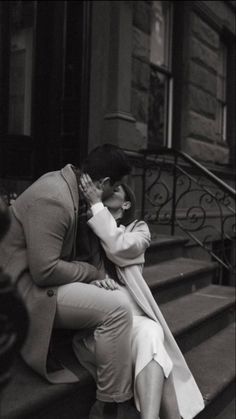 a man kissing a woman on the cheek while sitting on some steps in front of a building