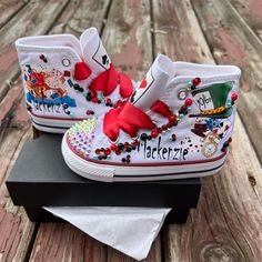 a pair of white shoes with red bows and beads on them sitting on top of a black box