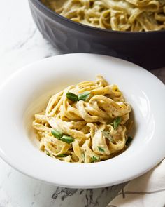 a white bowl filled with pasta and sauce next to a skillet full of noodles