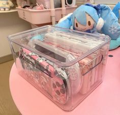 a pink table topped with a plastic container filled with lots of stuff next to a stuffed animal