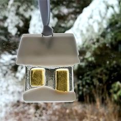 a glass ornament with two yellow squares hanging from it's side in front of snow covered trees