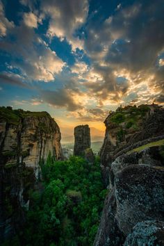 the sun is setting over some rocks and green trees in the foreground, as seen from an overlook point