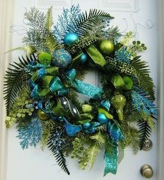 a christmas wreath with blue and green decorations on the front door, next to a white door