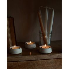 three candles sitting on top of a wooden table next to a book and glass vase