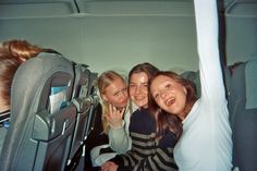 three women are sitting on an airplane with their arms around each other as they look at the camera