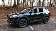 a black toyota rav is parked in a parking lot with trees and leaves on the ground