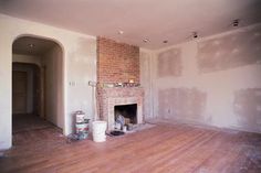 an empty living room with white walls and wood flooring in the foreground is a brick fireplace