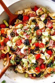 a bowl filled with pasta salad next to a wooden spoon