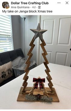 a wooden christmas tree on top of a white table with a red and black bow