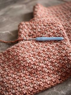 a crocheted pink tie with a blue button on it's end and a needle in the middle