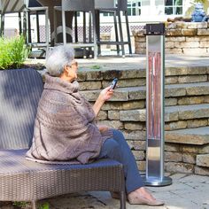 an older woman sitting on a bench next to a heater and looking at her cell phone