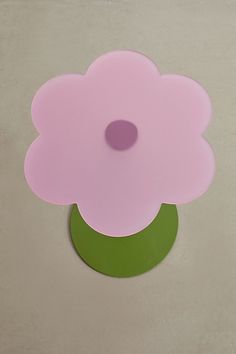 a pink flower sitting on top of a green stand next to a white wall and floor