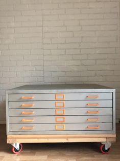 a grey and orange dresser sitting on wheels in front of a white brick wall with red handles