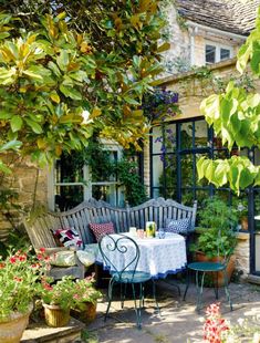 an outdoor table and chairs in front of a house with potted plants on the patio