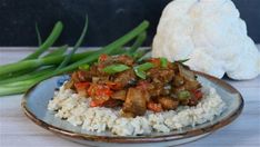 a plate with rice and meat on it next to some green onions in the background