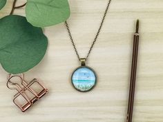 a close up of a necklace on a table next to a pen and some leaves