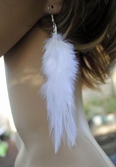 a close up of a woman's head wearing earrings with white feathers on it