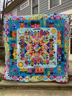 a colorful quilt hanging on the side of a house