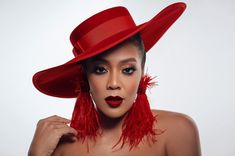 a woman wearing a red hat with feathers around her neck and eyeshadow, posing for the camera