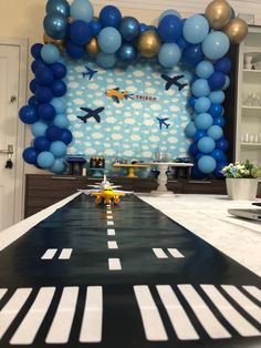 an airplane themed birthday party with blue and gold balloons, white tablecloths and black runner