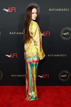 a woman standing on top of a red carpet wearing a gold and green dress with colorful stripes