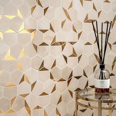 a vase with reeds on a table in front of a wall that has geometric tiles