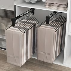 two racks with clothes hanging on them in front of a white shelf filled with folded towels