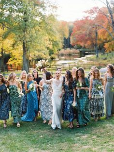 a group of women standing next to each other in front of trees and grass holding bouquets