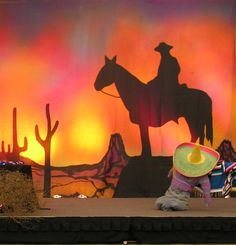 a stage set up for a show with a cowboy on horseback and cactus in the background